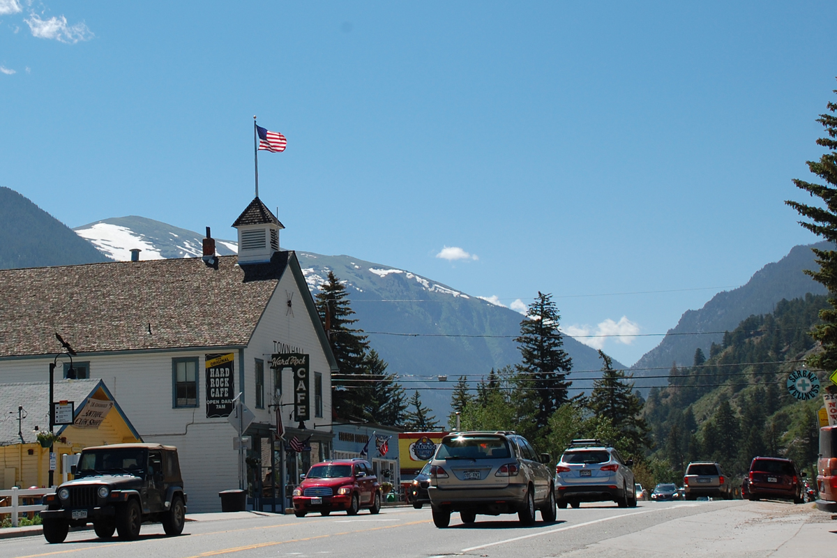 An old white building with a flag on top is on a quiet street with mountains in the background inEmpire, Colorado