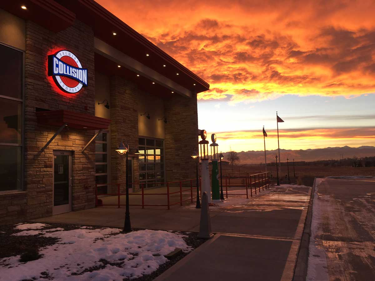 Collision Brewery Comapny sits on the left with with mountain views to the right. The sun is setting and the clouds in the sky are orange and yellow above the icy parking lot.