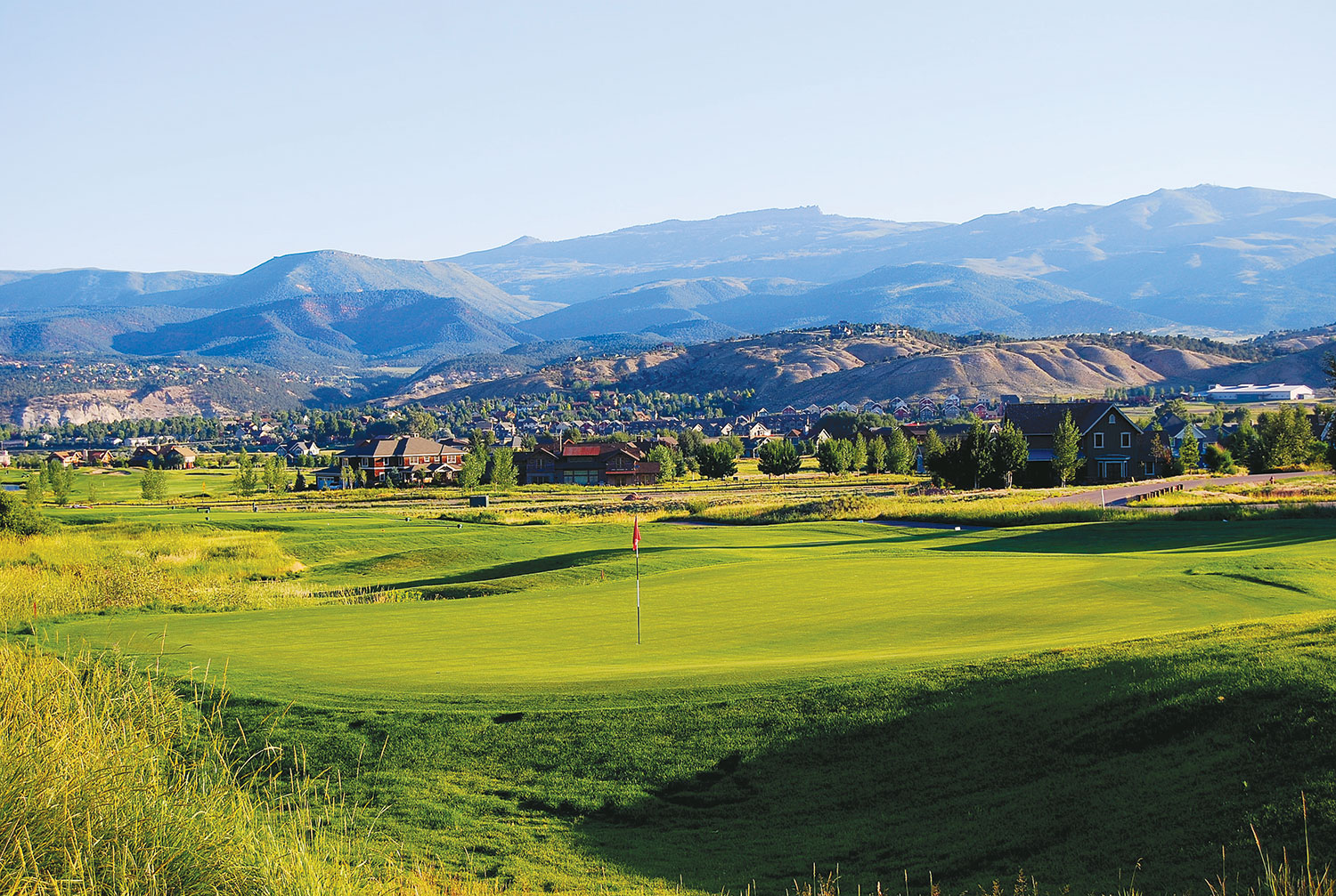 The rolling green course of Eagle Ranch Golf Course sits peacefully beneath distant, majestic, blue-and-purple mountains.