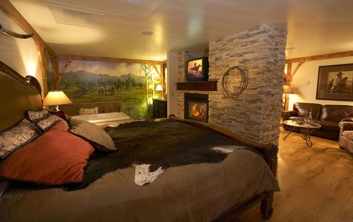 A bed piled in pillows with a fireplace at the foot in a hotel room with wooden western accents