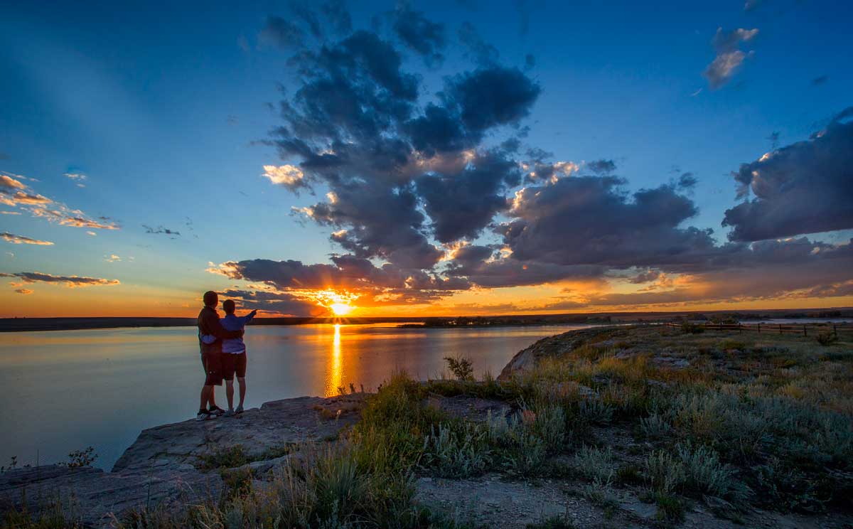 Two people walk along the shore of North Sterling State Park at sunset