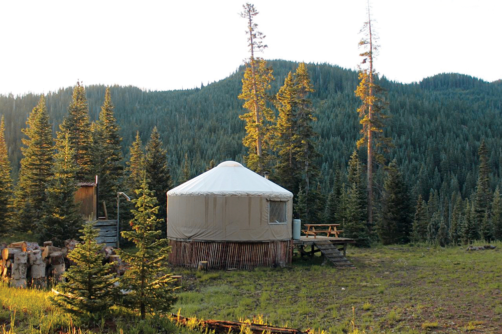 A round white yurt with a tented top and a fabric window sits on a raised wooden platform in the backcountry near Pagosa Springs.