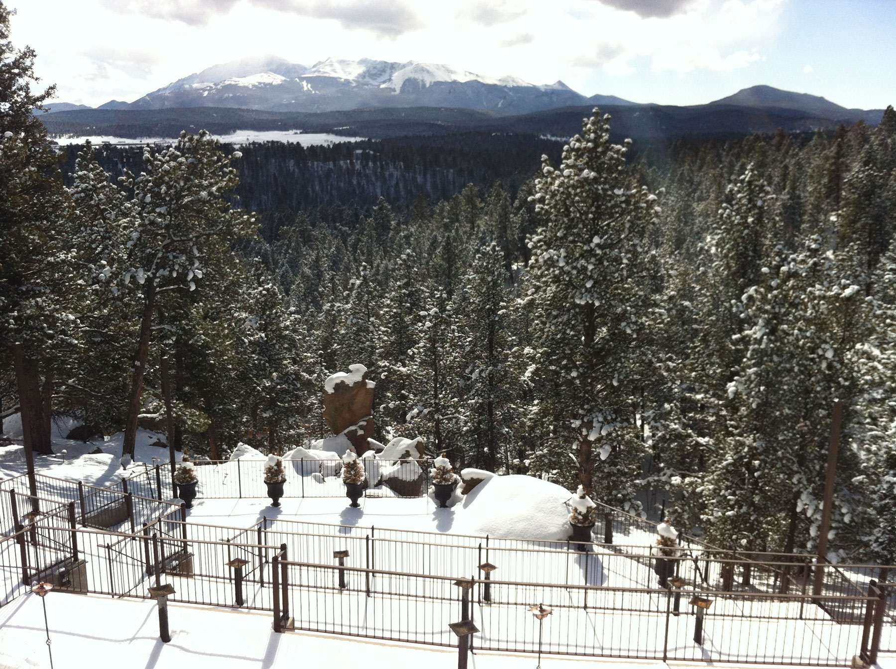 A valley lies thick with evergreen pines outside a bed and breakfast in Woodland Park, Colorado. The trees and patio area are covered with a layer of fresh snow.