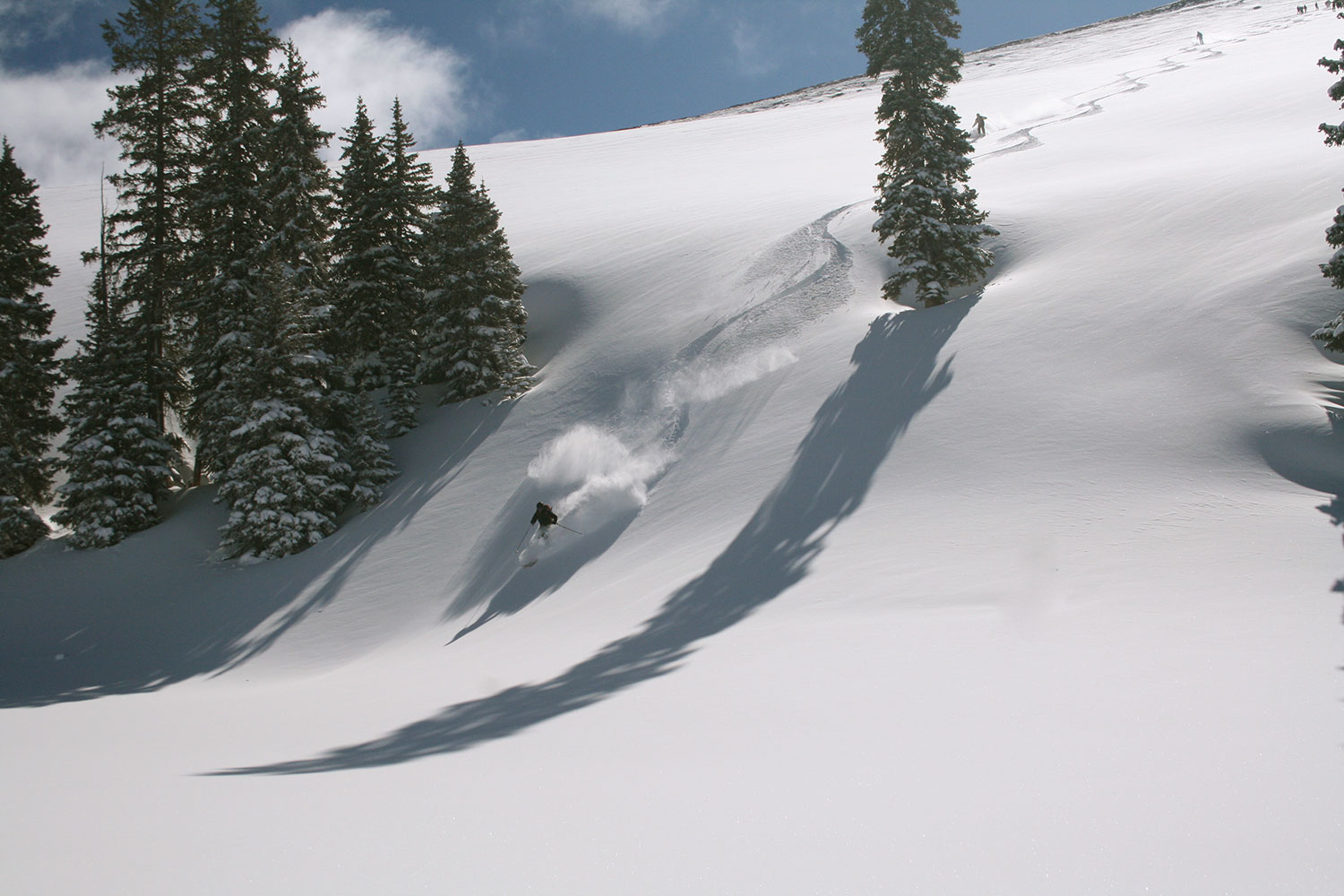 A skier makes the first set of tracks and leaves behind clouds of powder on an untouched snowy slope near Vail, Colorado.