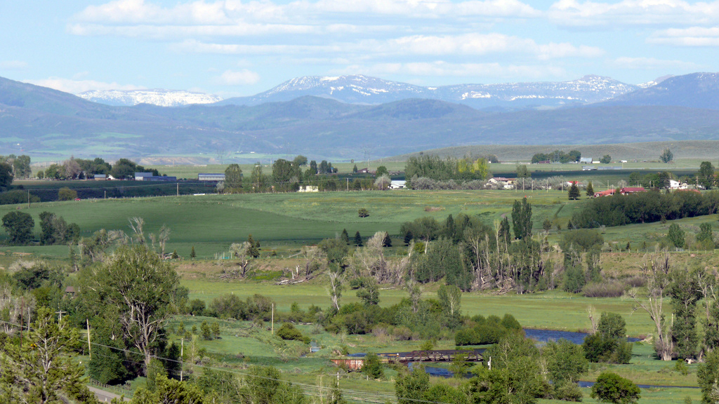 A view of the green White River Valley with snowcapped mountains sitting under puffy white clouds in the distance.