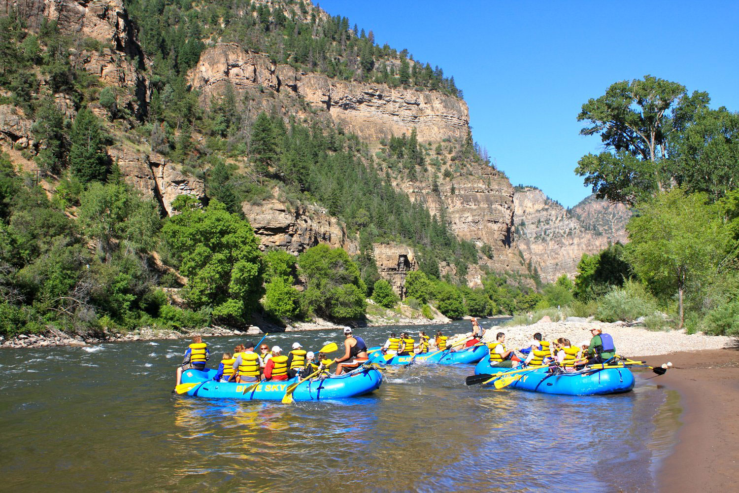 Three rafts filled with people rest on the Colorado River during a rafting tour