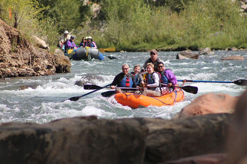 a group of people in life jackets smile as the whitewater raft on the Animas River