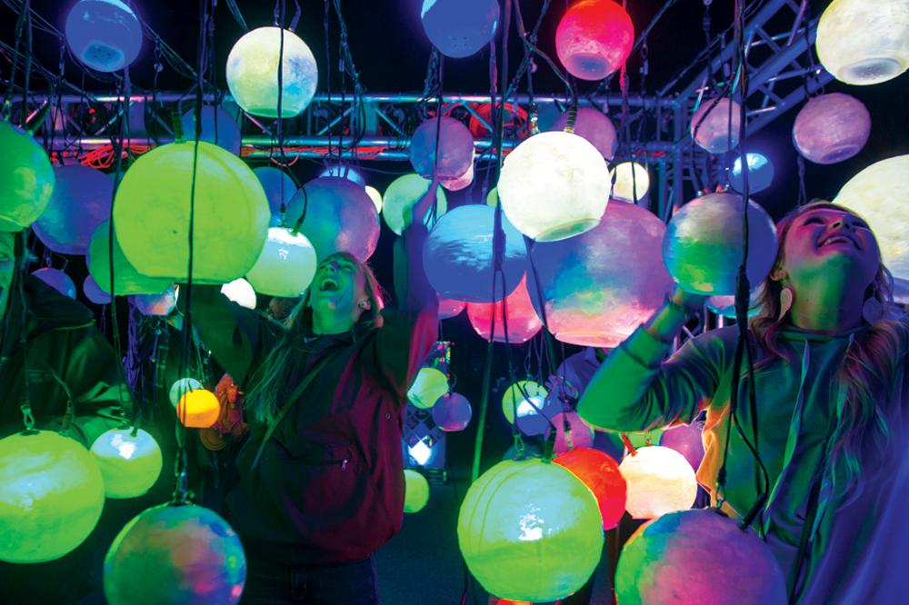 Two people smile widely amid dozens of multi-colored, glowing spheres at the Breckenridge International Festival of Arts.