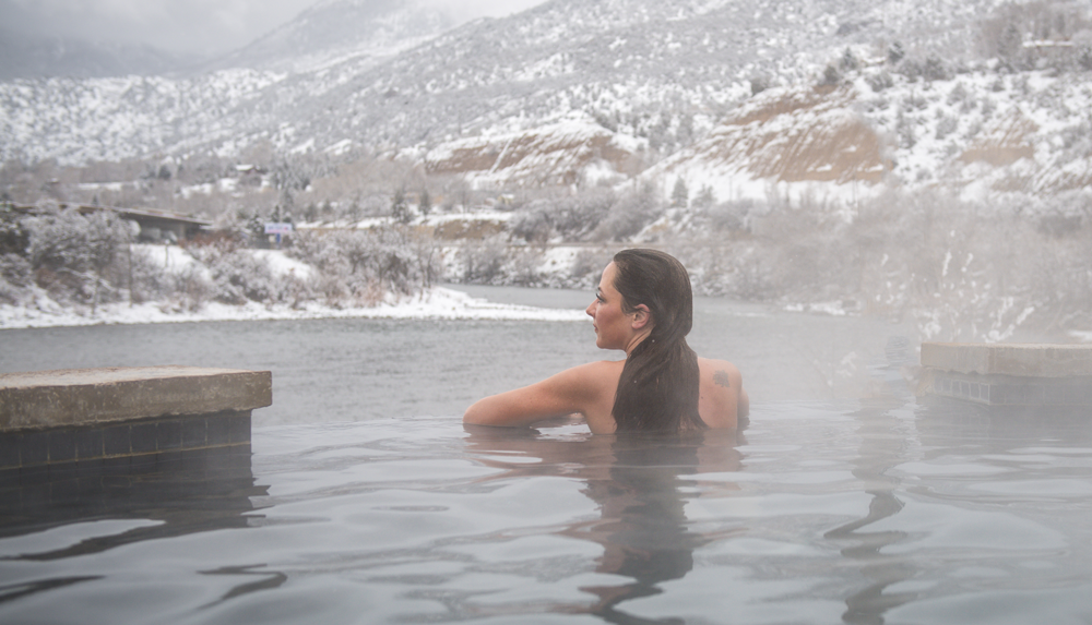 A woman soaks in hot springs while looking out over snowy mountains
